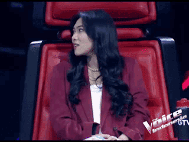 a woman in a red jacket is sitting in a red chair with the word voice indonesia written on it