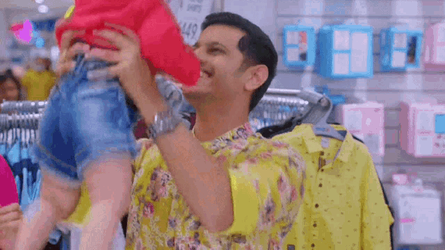 a man in a yellow shirt is holding a baby in his arms in a store .