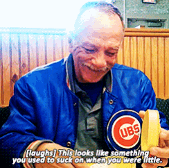 a man wearing a blue cubs jacket laughs while holding a banana