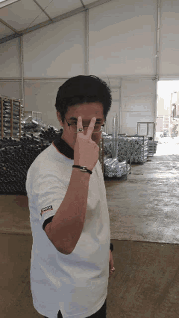 a man wearing glasses and a white shirt that says ' toyota ' on it is giving the peace sign