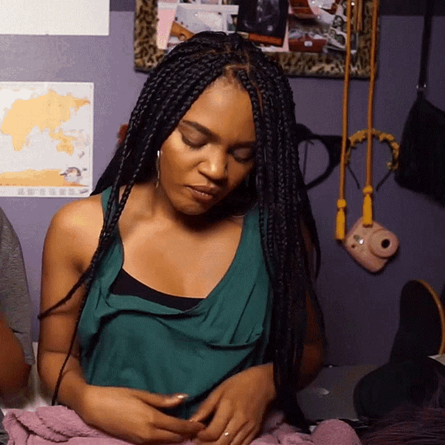 a woman with braids is sitting in front of a purple wall with a map of the world on it