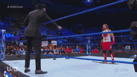 a man in a suit is standing in a wrestling ring with a wrestler