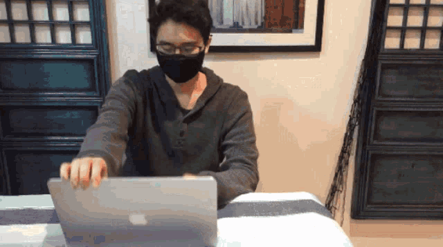 a man wearing glasses and a black mask is using an apple laptop