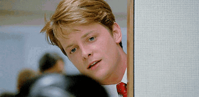 a young man in a suit and tie is peeking out from behind a door .