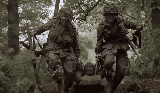 a group of soldiers are walking through the woods carrying a man on a stretcher