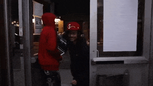 a man in a red hoodie and a red hat is standing in a doorway .