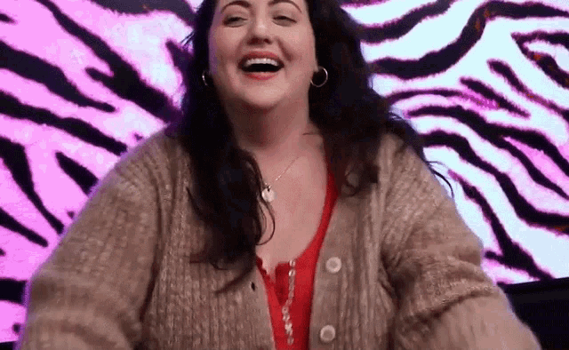 a woman in a sweater is laughing in front of a pink and black zebra print background .