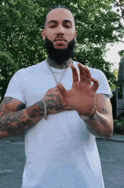 a man with a beard and tattoos is wearing a white t-shirt and gold chains .