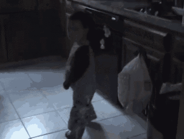 a little girl is standing in a dark kitchen with a bag on the floor
