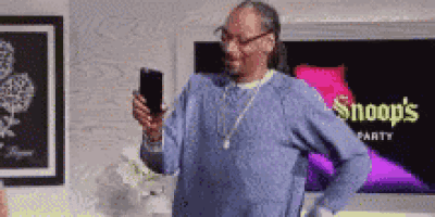 snoop dogg is holding a cell phone in his hand while standing in a room .