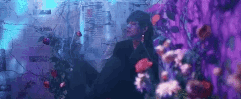 a man is standing in front of a wall surrounded by purple flowers .