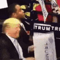 a man in a suit and tie is holding a sign that says trump on it .