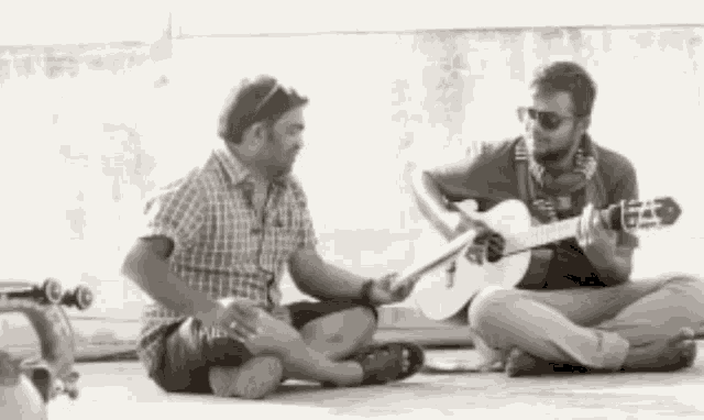 two men are sitting on the ground one is playing a guitar and the other is singing