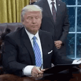donald trump is sitting at a desk with his eyes closed while holding a clipboard .