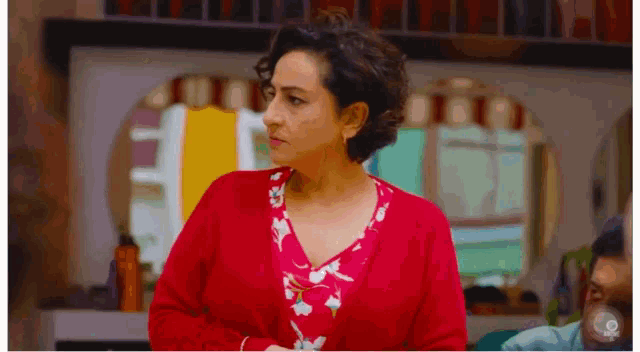 a woman wearing a red cardigan and a floral shirt stands in a room