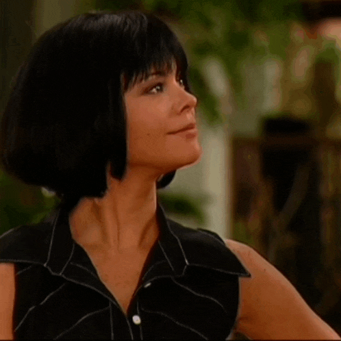 a woman with short black hair is smiling and wearing a black sleeveless shirt