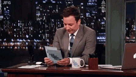 a man is sitting at a desk with a mug that says jimmy fallon