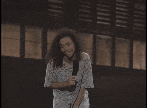 a woman in a lace dress is singing into a microphone in front of a building