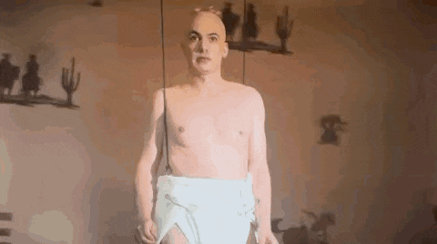 a bald man is standing in a room with a diaper on his waist .