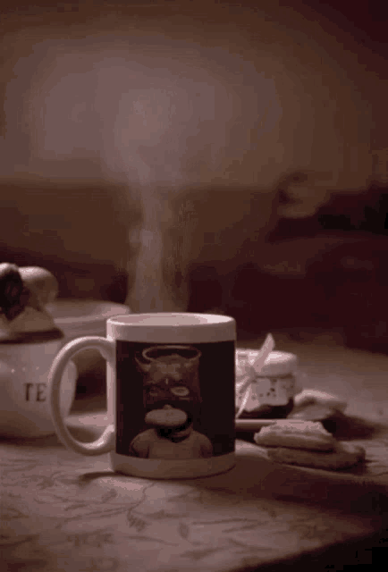 a mug with a cat on it sits on a table next to a tea pot