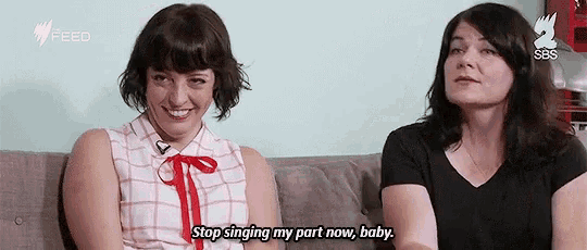 two women are sitting on a couch and one of them is singing .