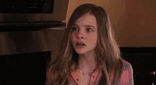 a young girl is making a funny face in front of a microwave in a kitchen .
