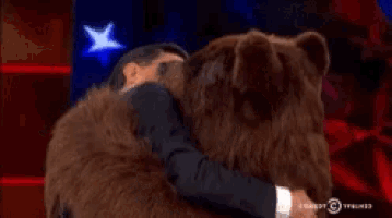 a man in a suit is hugging a stuffed bear with comedy central written on the bottom