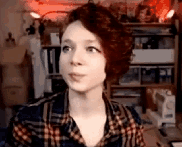a woman with red hair is wearing a plaid shirt and making a face .