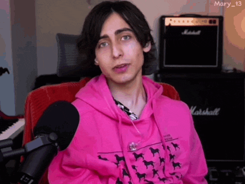 a young man wearing a pink hoodie is sitting in front of a marshall amplifier