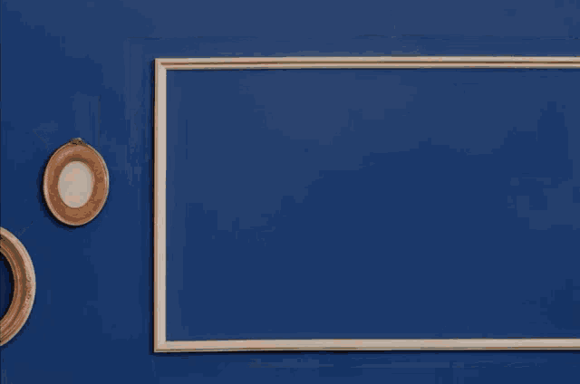 a young man in a white shirt is standing in front of a blue wall with his mouth open .