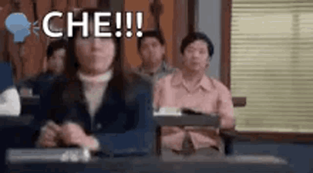 a group of people are sitting at desks in a classroom with the words `` che !!! '' written on the screen .