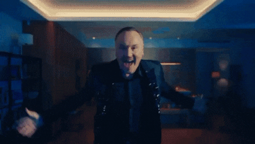 a man is dancing in a living room with his arms outstretched and a mustache .