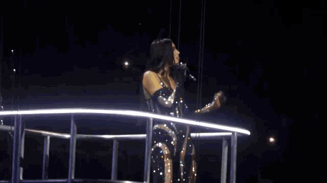 a woman in a sequined dress is standing on a stage with her arms outstretched .