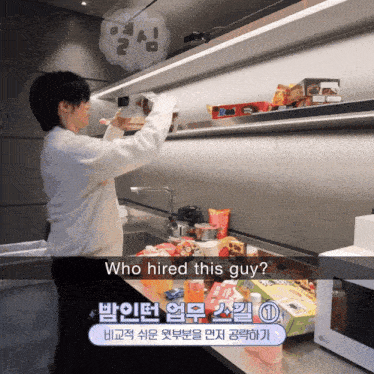 a man in a white sweater is standing in a kitchen with a sign that says " who hired this guy "