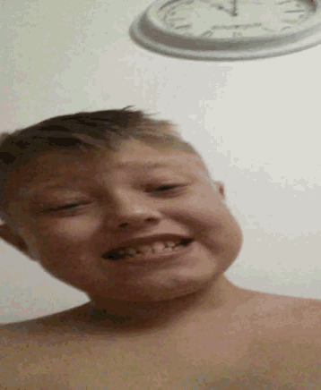 a young boy is smiling in front of a wall clock that shows the time as 7:15