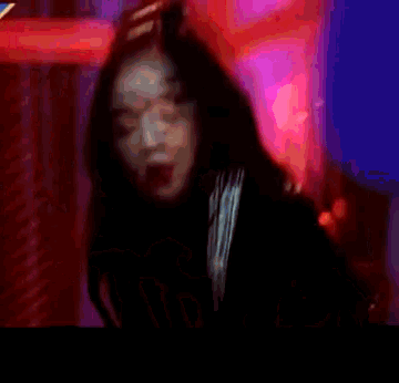 a woman is standing in front of a red light and making a peace sign with her hand .