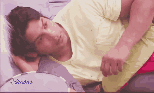 a man in a yellow shirt is laying on a bed with the words " shubhs " on the bottom right