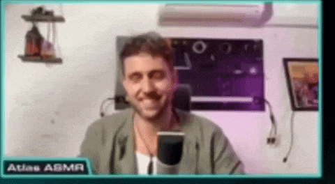 a man is smiling in front of a microphone while sitting in front of a screen that says atlas asmr .