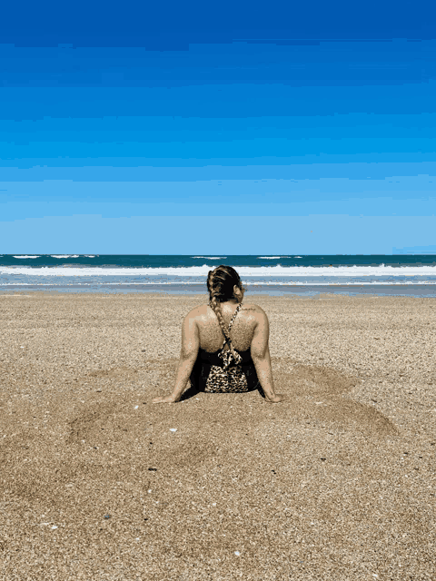 a woman in a leopard print bathing suit sits in the sand on a beach