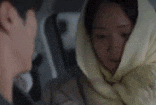 a woman is sitting in a car with a scarf wrapped around her head .