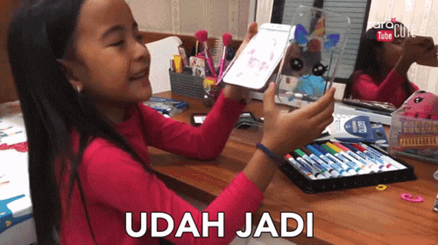 a little girl holding a piece of paper that says udah jadi on the bottom