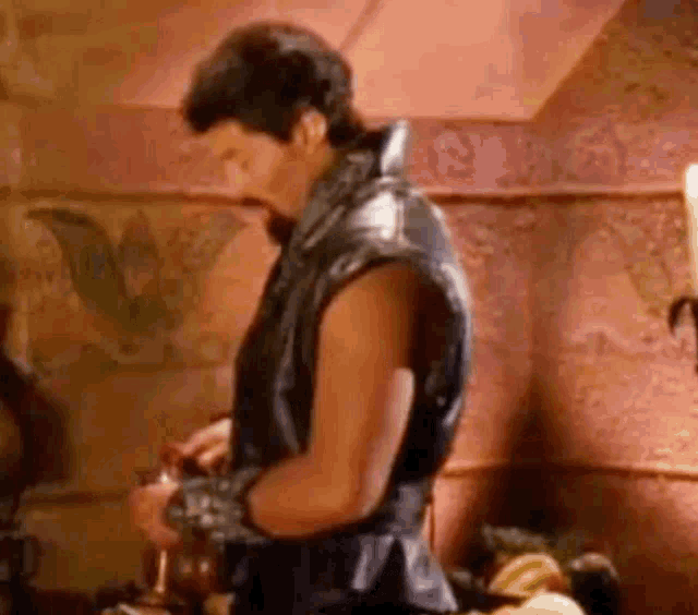 a man in a leather vest is standing in a room holding a bottle .