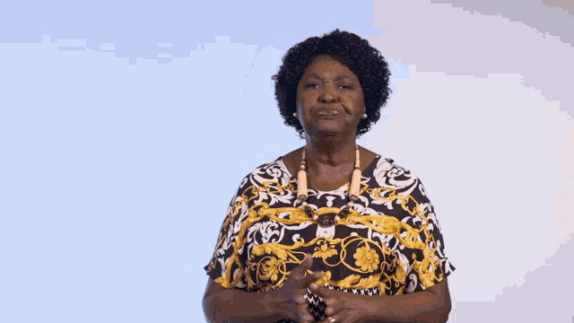an elderly woman wearing a yellow and black shirt holds her hands out