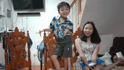 a woman sits next to a young boy who is standing on a chair