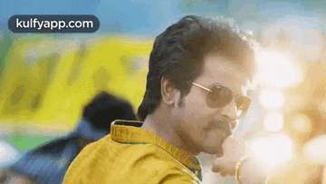 a man wearing sunglasses and a yellow shirt is standing in front of a yellow bus .