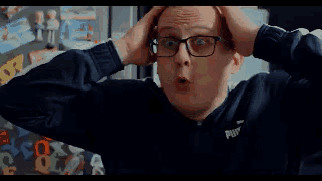 a bald man wearing glasses and a blue puma jacket is talking on a cell phone .