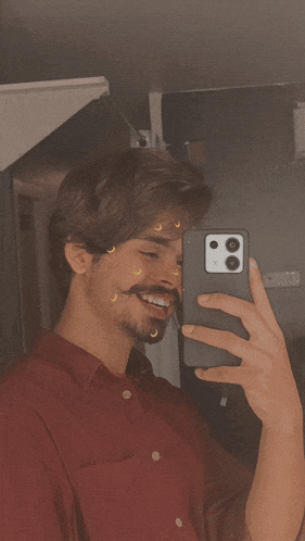 a man in a red shirt is taking a picture of himself with his phone