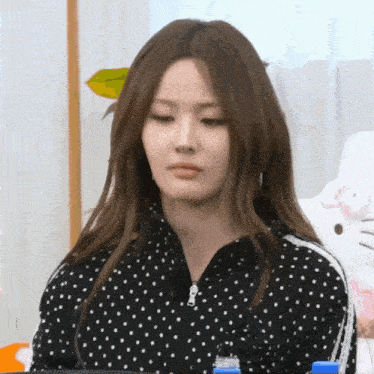 a woman wearing a black polka dot jacket is sitting in front of a hello kitty doll .