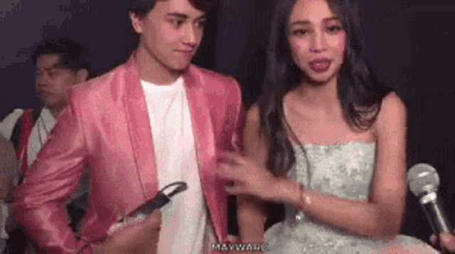 a man in a pink jacket and a woman in a white dress are standing next to each other .