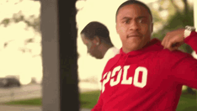 a man wearing a red polo hoodie stands in front of another man